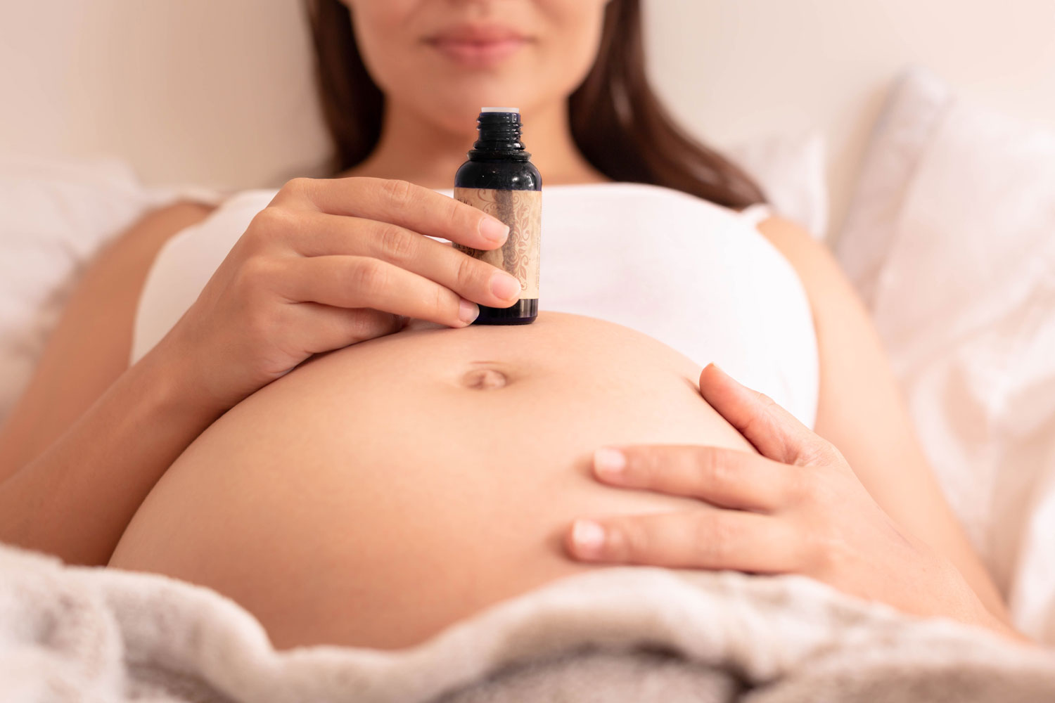 mujer embarazada con fraso de aceite esencial encima de su barriga